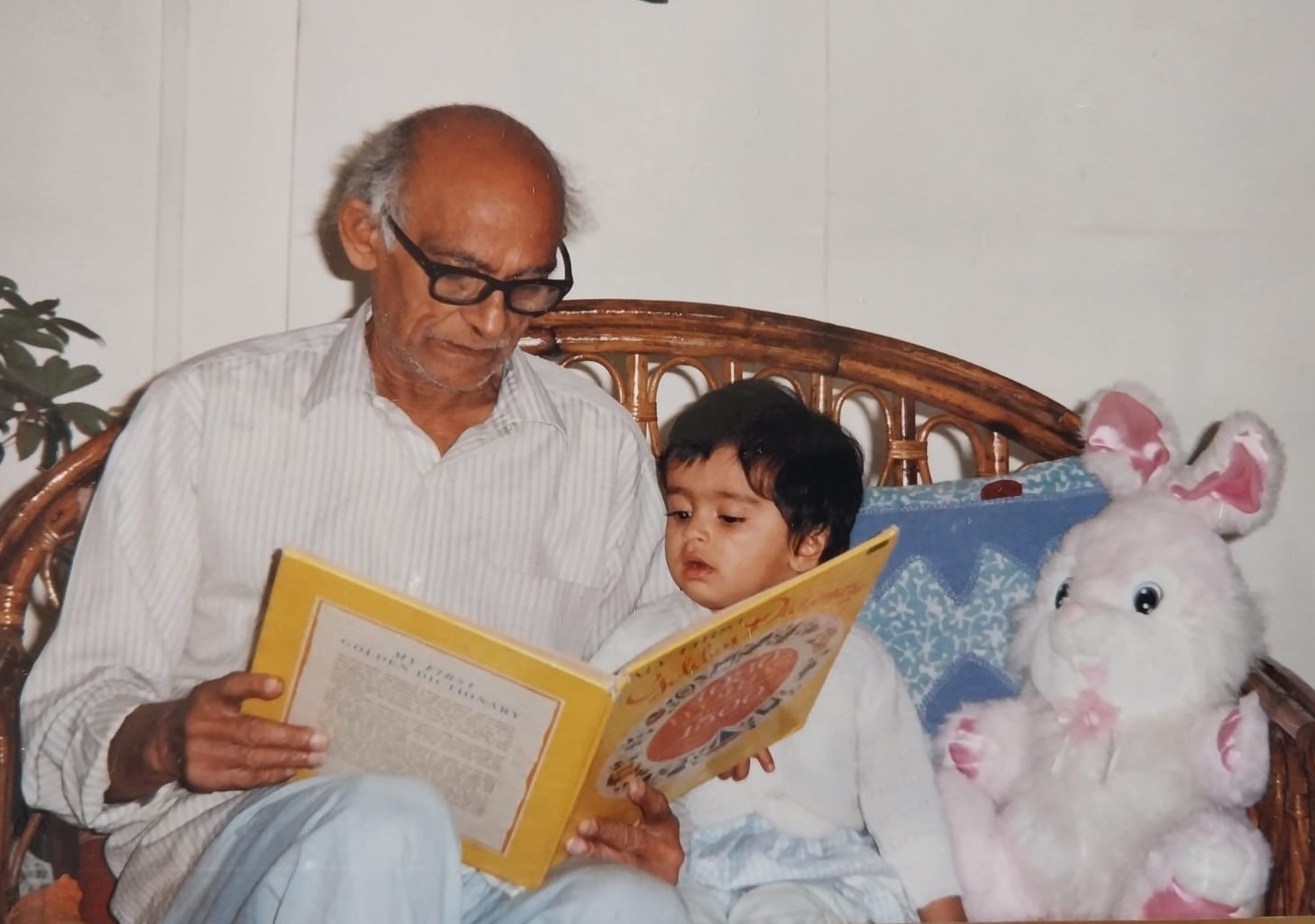 A grandfather reading a picture book with a young child seated beside him.