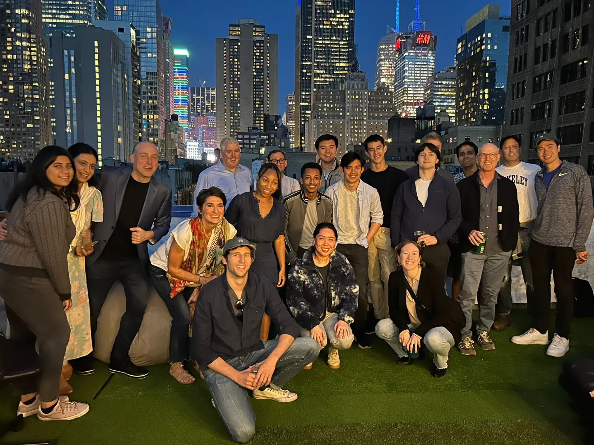 A group of colleagues and friends gathered on a rooftop terrace with the New York City skyline behind them.